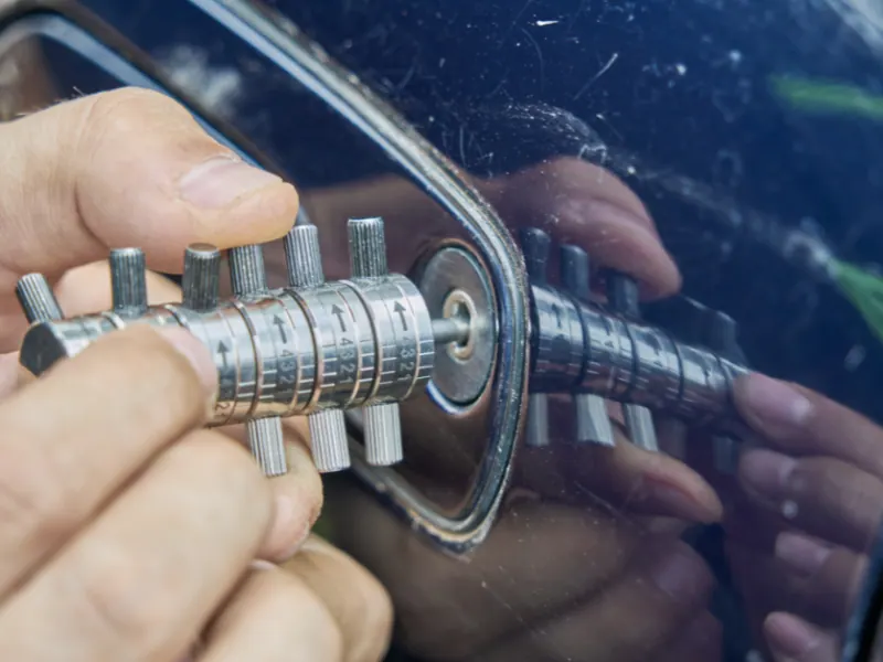 Person using a combination lock tool on a car door lock, illustrating automotive locksmith services for car lockouts and key replacements.