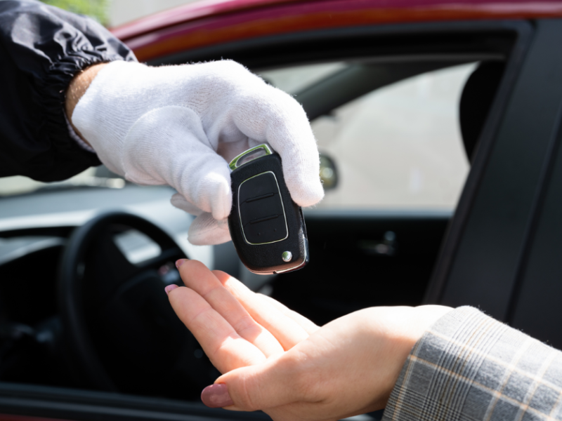 Automotive locksmith handing over a car key to a customer, emphasizing car key replacement services.
